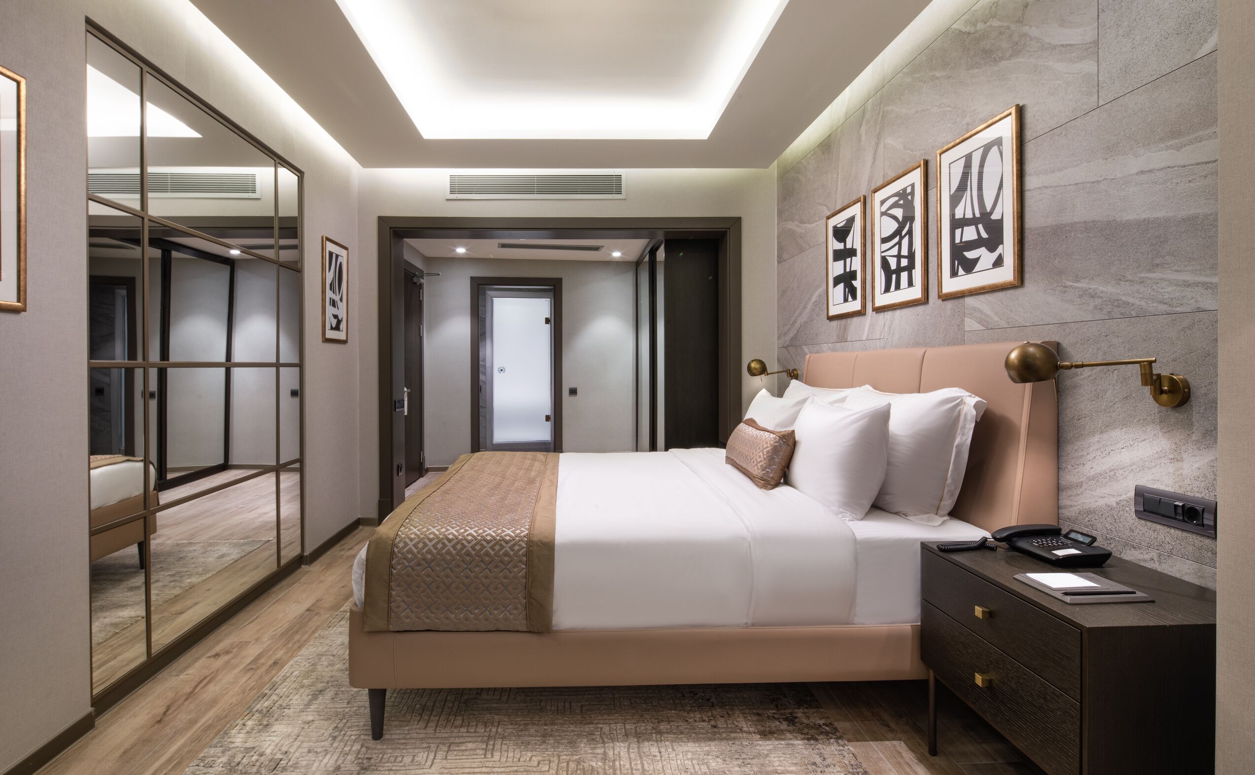 A modern bedroom with a large bed, bedside tables, a wardrobe, and artwork on the walls.