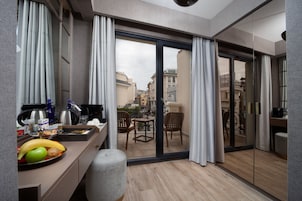 Una habitación de hotel moderna con balcón, una zona de comedor con productos para el desayuno y vistas a la ciudad.