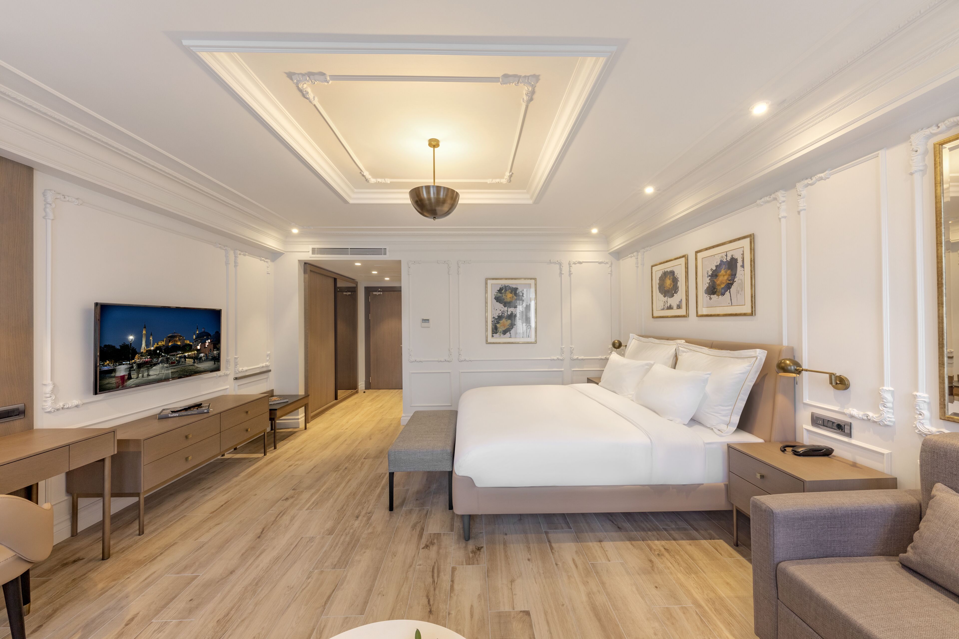 A modern hotel room with a large bed, a desk, a TV, and a seating area.
