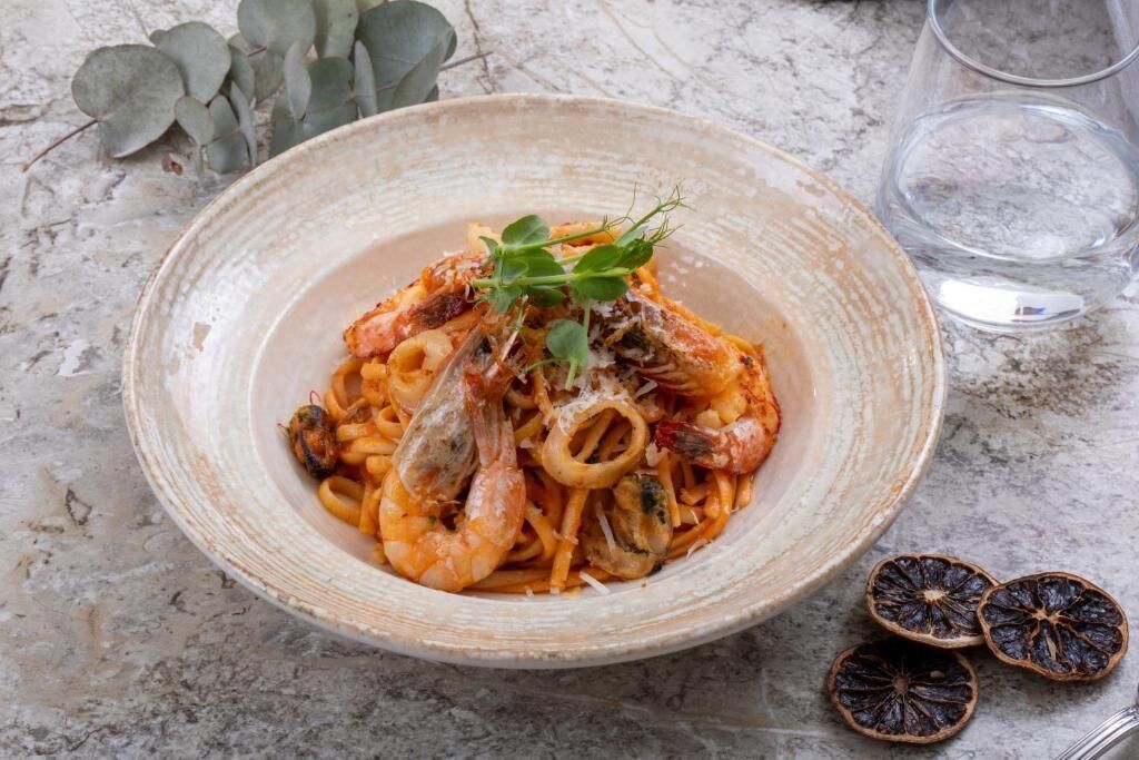 A bowl of pasta with shrimp and squid, garnished with herbs, on a marble surface.
