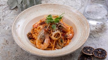 A bowl of pasta with shrimp and squid, garnished with herbs, on a marble surface.