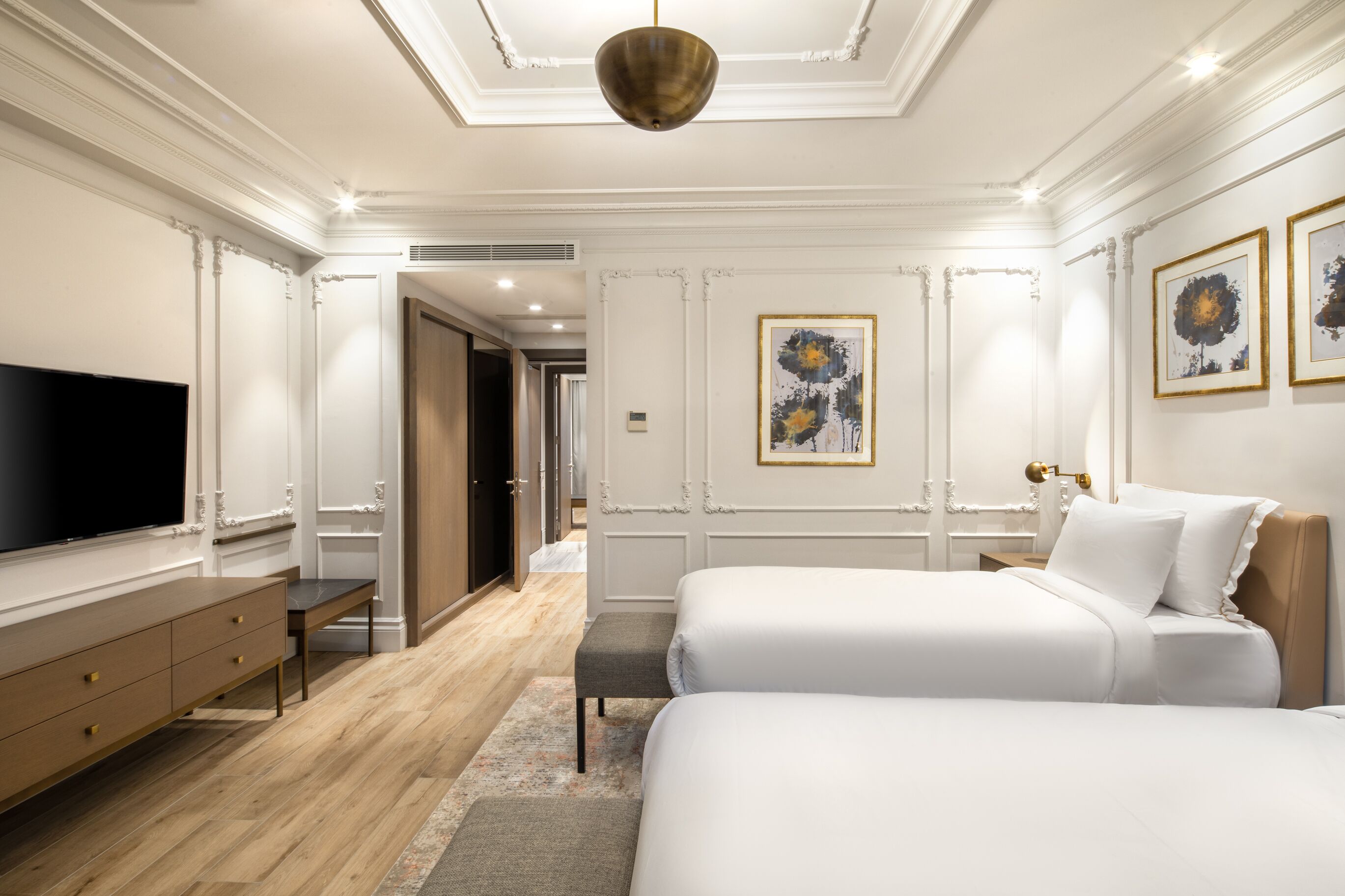 A hotel room with two beds, a TV, a wooden dresser, and artwork on the walls.