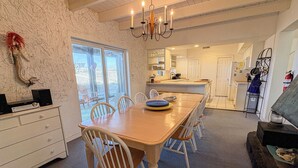 Un comedor con una mesa y sillas de madera, una araña y vista a la cocina.