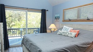 A bedroom with a bed, a window with blinds, a balcony with a chair, and a lamp. - 🏖️Anchored Inn - updated 4BR/3BA Oceanside home w/Private Pool 🏖️ (Corolla)