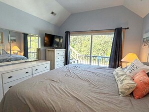A bedroom with a large bed, a TV, a dresser, and a balcony with a view of trees. - 🏖️Anchored Inn - updated 4BR/3BA Oceanside home w/Private Pool 🏖️ (Corolla)