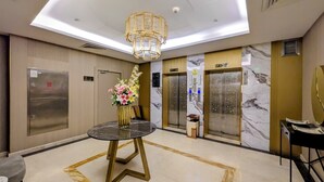 A hotel lobby with a marble floor, a round table with a vase of flowers, and two elevators. - Al Mansour Plaza Hotel (Doha)