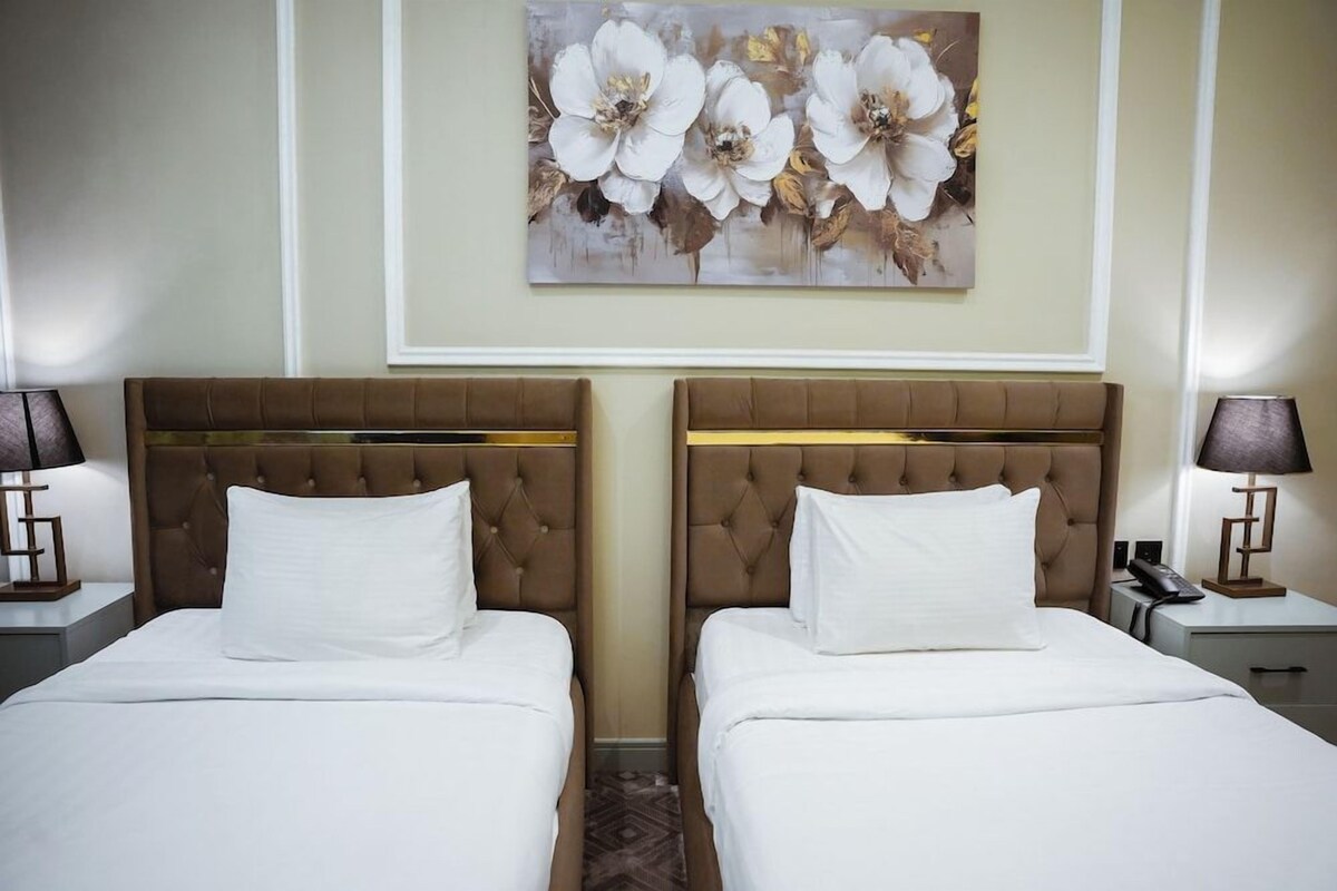 A hotel room with two beds, a painting of flowers on the wall, and bedside lamps.