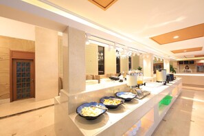 A modern hotel lobby with a reception desk, a seating area, and a buffet with bowls of fruit.