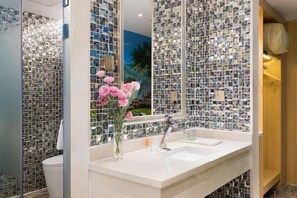 A bathroom with a tiled wall, a sink, and a mirror.