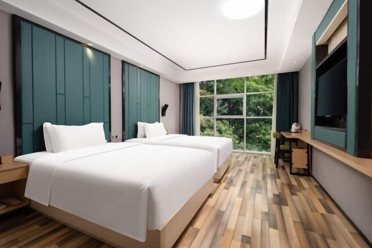 Habitación de hotel moderna con dos camas, televisión, una mesita y un ventanal con vistas a zonas verdes.