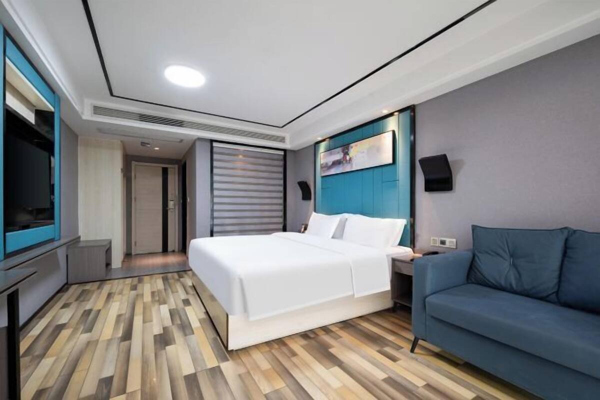 Una habitación de hotel moderna con una cama grande, un sofá azul, un televisor de pantalla plana y piso de madera.