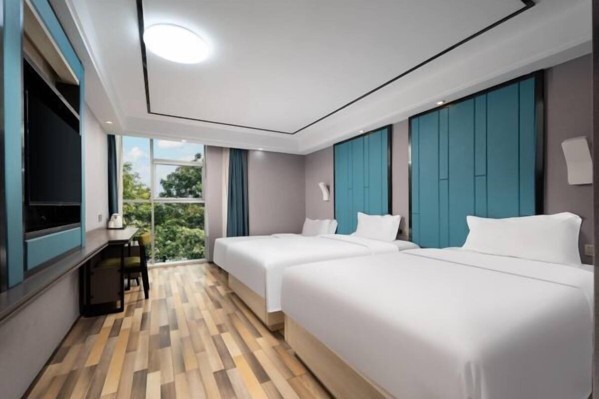 Habitación de hotel moderna con dos camas, televisor, escritorio y vista a zonas verdes.