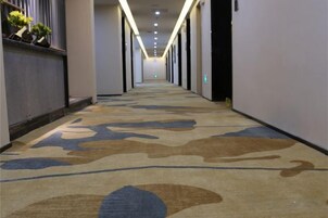 Un pasillo de hotel con alfombra estampada, puertas a ambos lados y una fuente de luz al final.