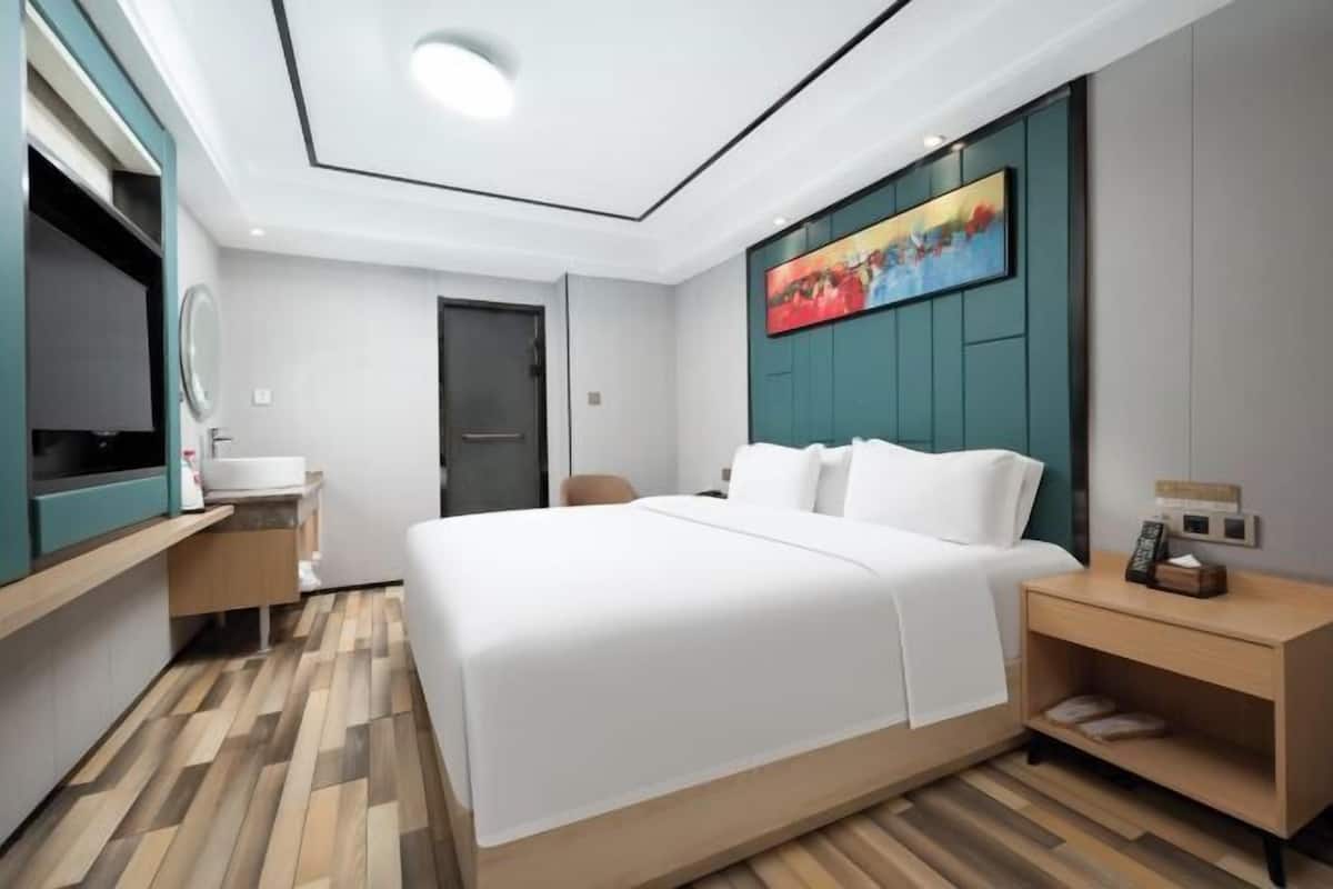 Una habitación de hotel moderna con una cama grande, una mesita de noche, un televisor y un baño con espejo y lavamanos.