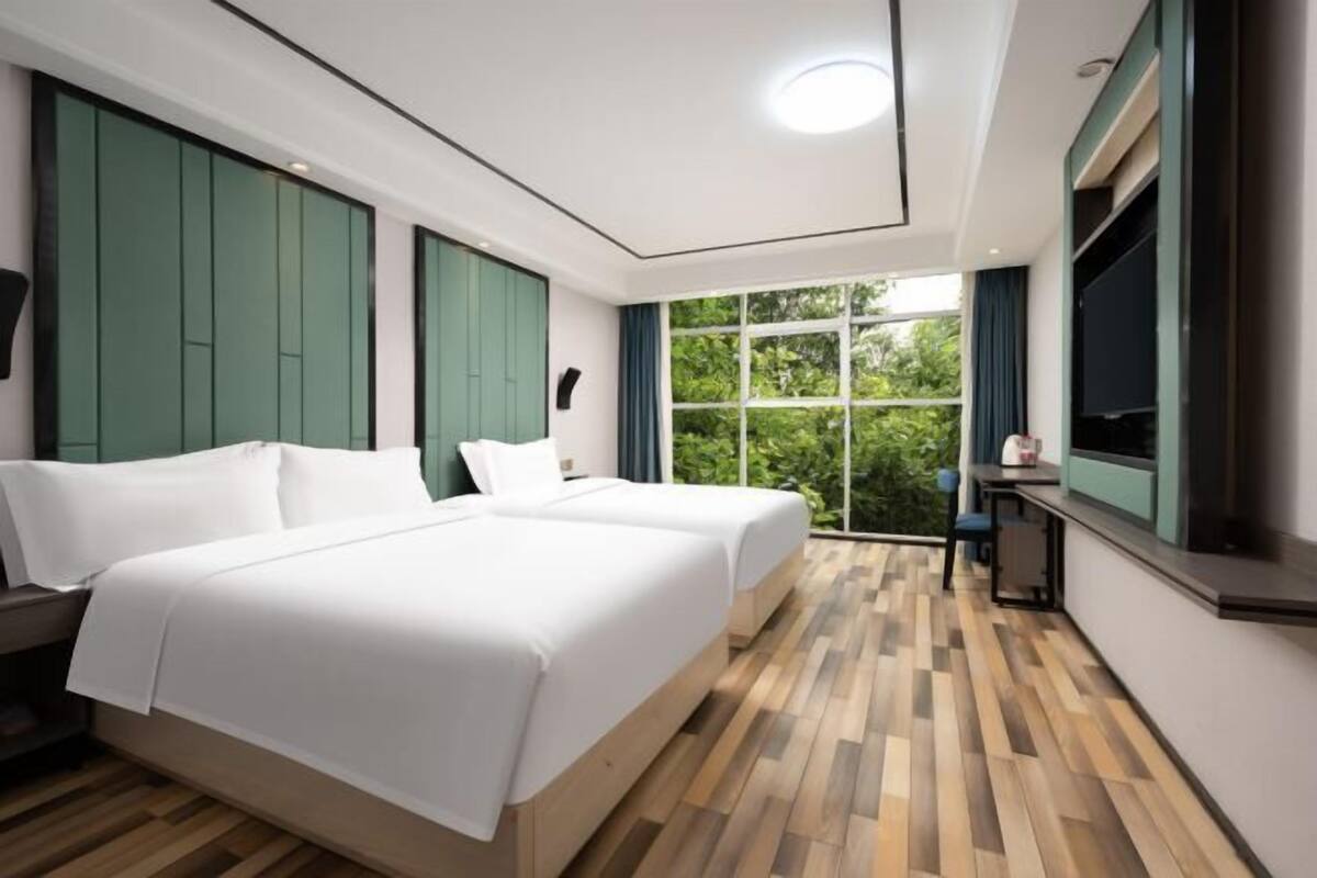 Habitación de hotel con dos camas, un ventanal grande y vistas a zonas verdes.