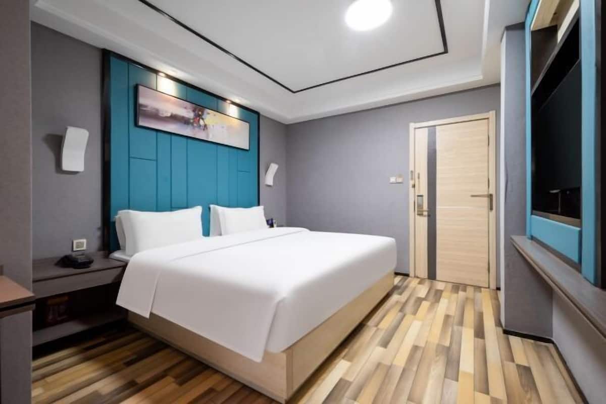 Una habitación de hotel moderna con una cama, una mesita de noche, un televisor montado en la pared y suelo de madera.