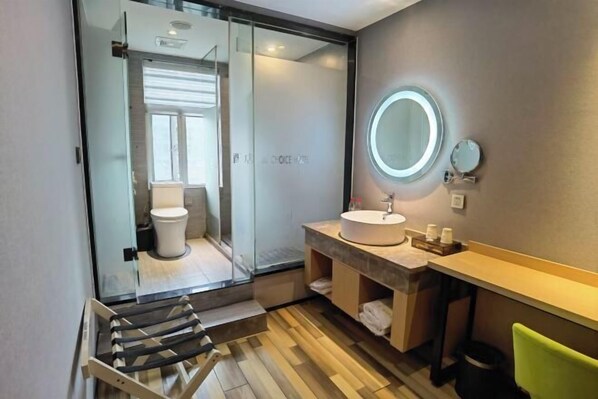 Une salle de bain moderne avec une douche à parois de verre, un miroir rond, un lavabo et un plancher en bois.