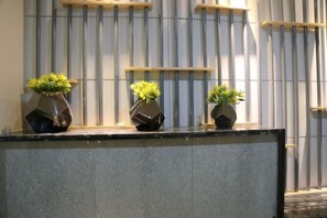 A reception desk with three potted plants and a vertical metal fence in the background.