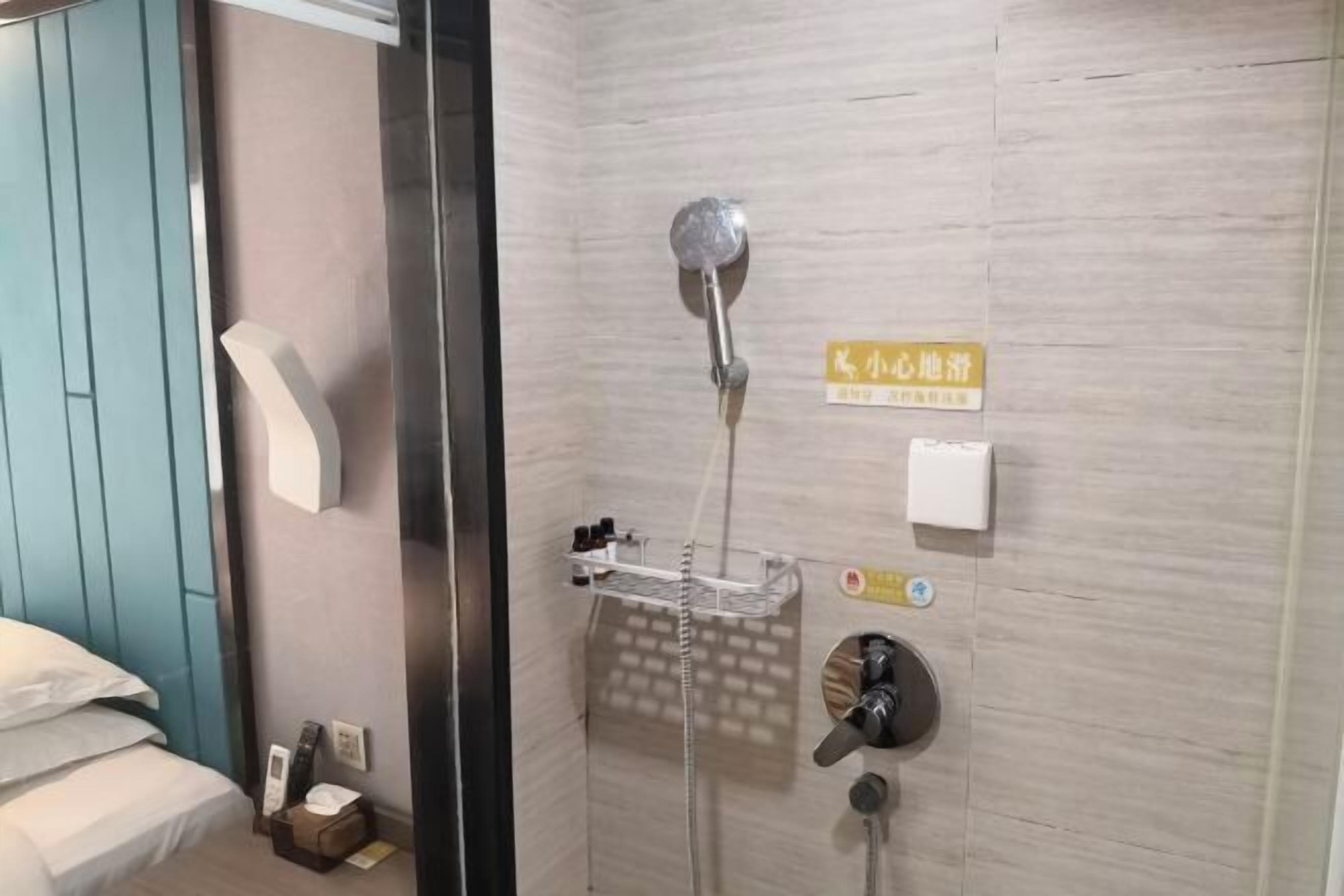 A hotel room with a shower, a bed, and a small bedside table with a tissue box.