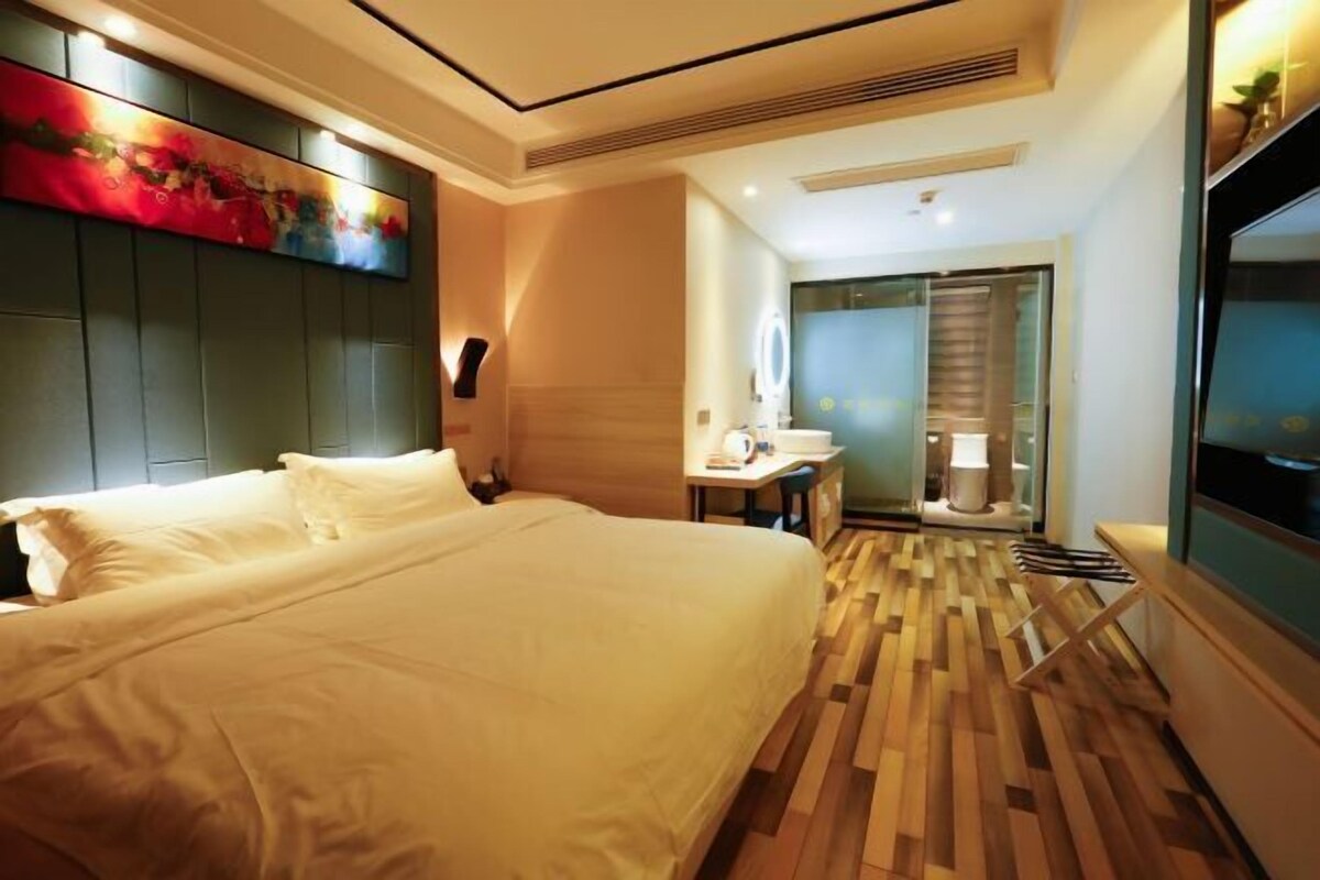 Une chambre d’hôtel avec un grand lit, un bureau avec une chaise, une télévision et une salle de bain équipée d’un miroir et de toilettes.
