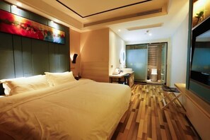 Une chambre d’hôtel avec un grand lit, un bureau avec une chaise, une télévision et une salle de bain équipée d’un miroir et de toilettes.