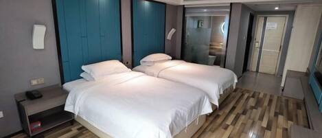 A modern hotel room with two beds, a wooden floor, teal accent walls, and a small bedside table with a phone.