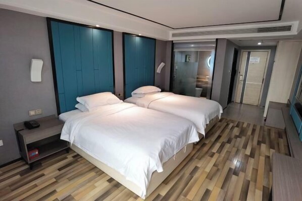 A modern hotel room with two beds, a wooden floor, teal accent walls, and a small bedside table with a phone.