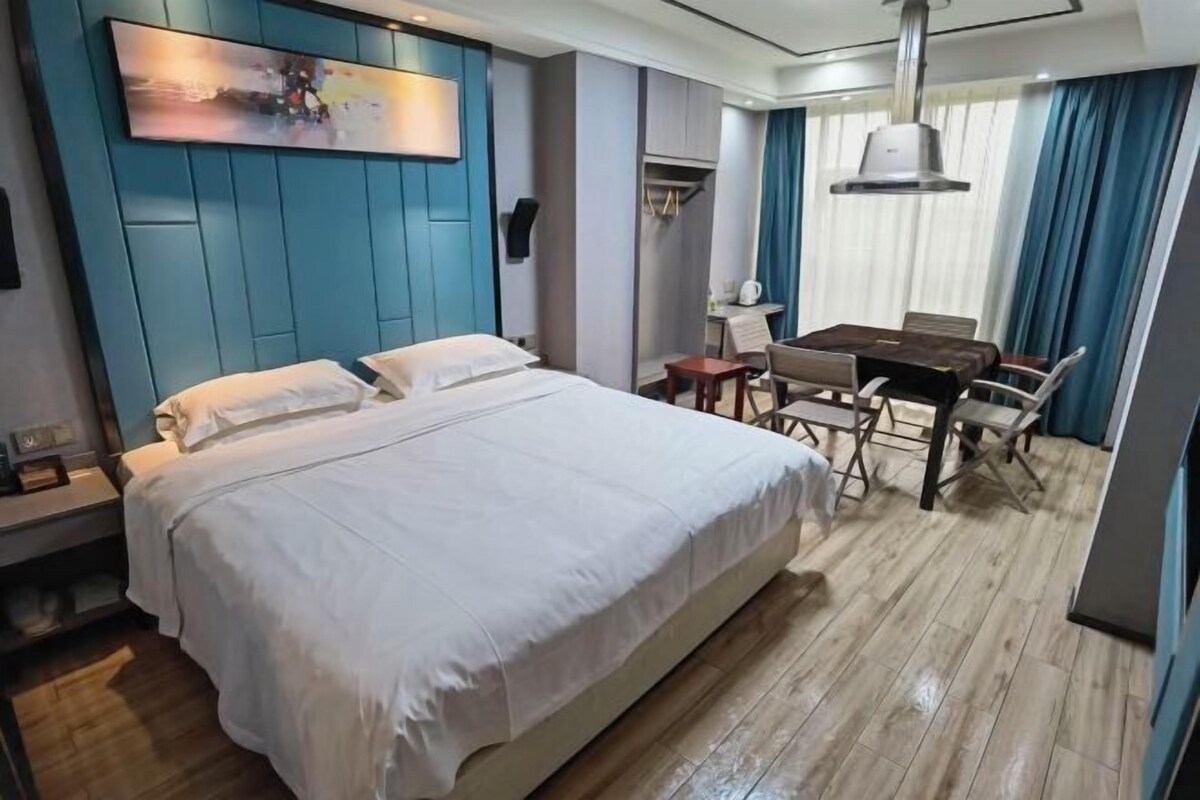 Une chambre d’hôtel avec un grand lit, un bureau avec des chaises, un tableau au mur et une fenêtre avec des rideaux.