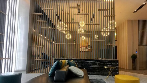 A modern living room with a sectional sofa, a yellow ottoman, and a decorative wall with vertical bars and hanging lights. - Mi Boutique Chain Hotel Xiantao (Xiantao)