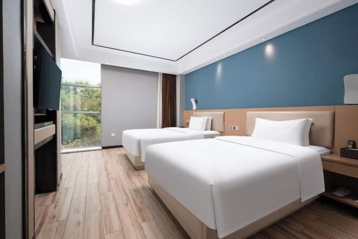 Habitación de hotel con dos camas, un balcón y vistas a zonas verdes.