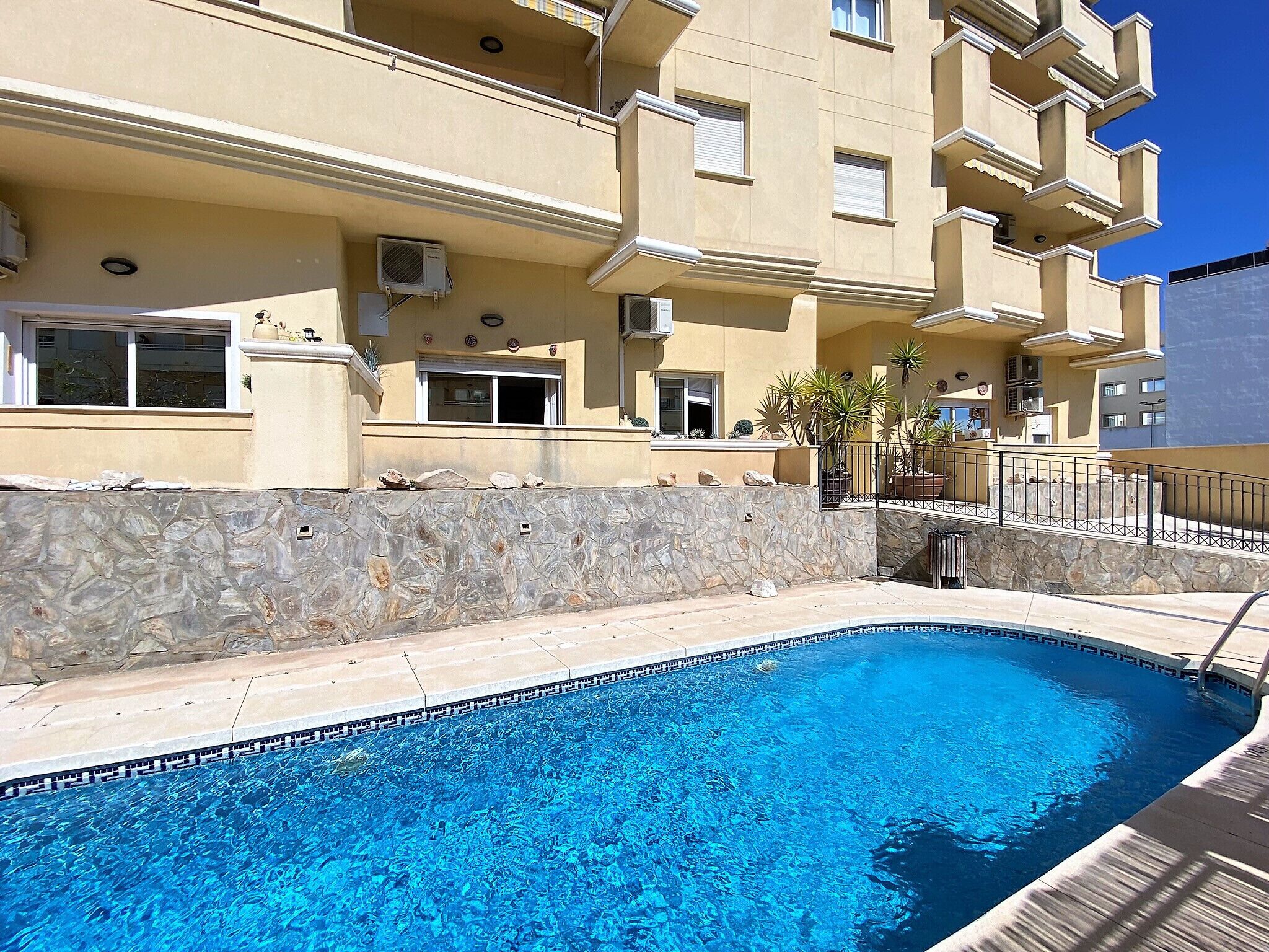Une piscine bordée d’un mur en pierre et un bâtiment doté de balcons et de fenêtres.