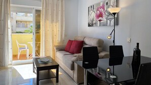 A modern living room with a sofa, a coffee table, a desk with a lamp, and a painting on the wall.