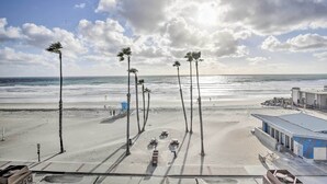 A beach view with palm trees, a lifeguard tower, and a building with a blue roof. - Charming Oceanside Condo w/ Beach & Pool Access! (Oceanside)