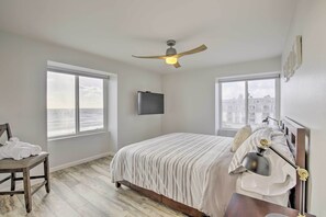 Ein Schlafzimmer mit Bett, Stuhl, Schreibtisch, Deckenventilator und großen Fenstern.