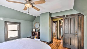 A bedroom with a bed, a ceiling fan, a window, a wooden door, and a hallway leading to another room. - Newly Renovated Home Close to Dtwn Lawrence! (Lawrence)