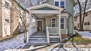A two-story house with a front porch, a stone wall on the left, and a snow-covered lawn. - Newly Renovated Home Close to Dtwn Lawrence! (Lawrence)