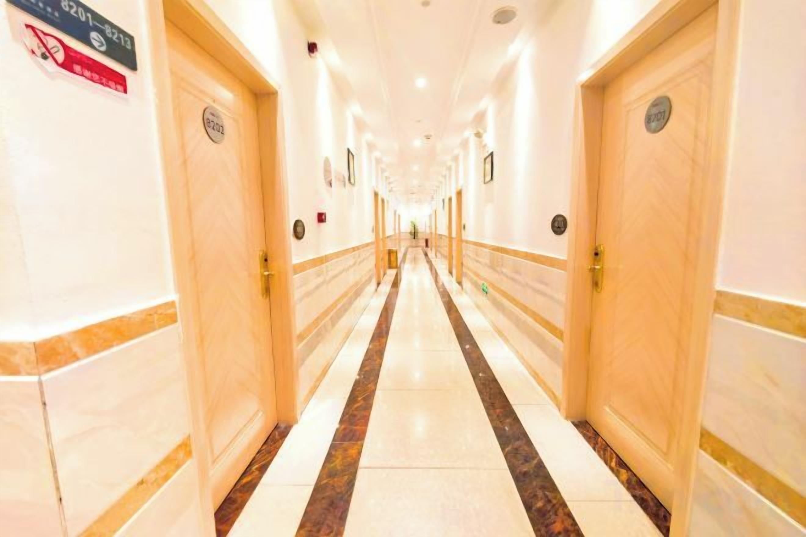 A hotel corridor with doors on both sides, a marble floor, and a sign on the left wall.