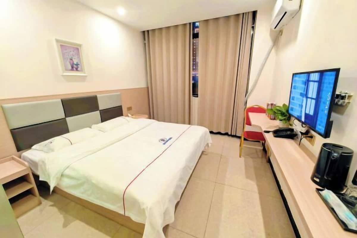 Hotellihuone, jossa on sänky, työpöytä tietokoneella, televisio ja kahvinkeitin.