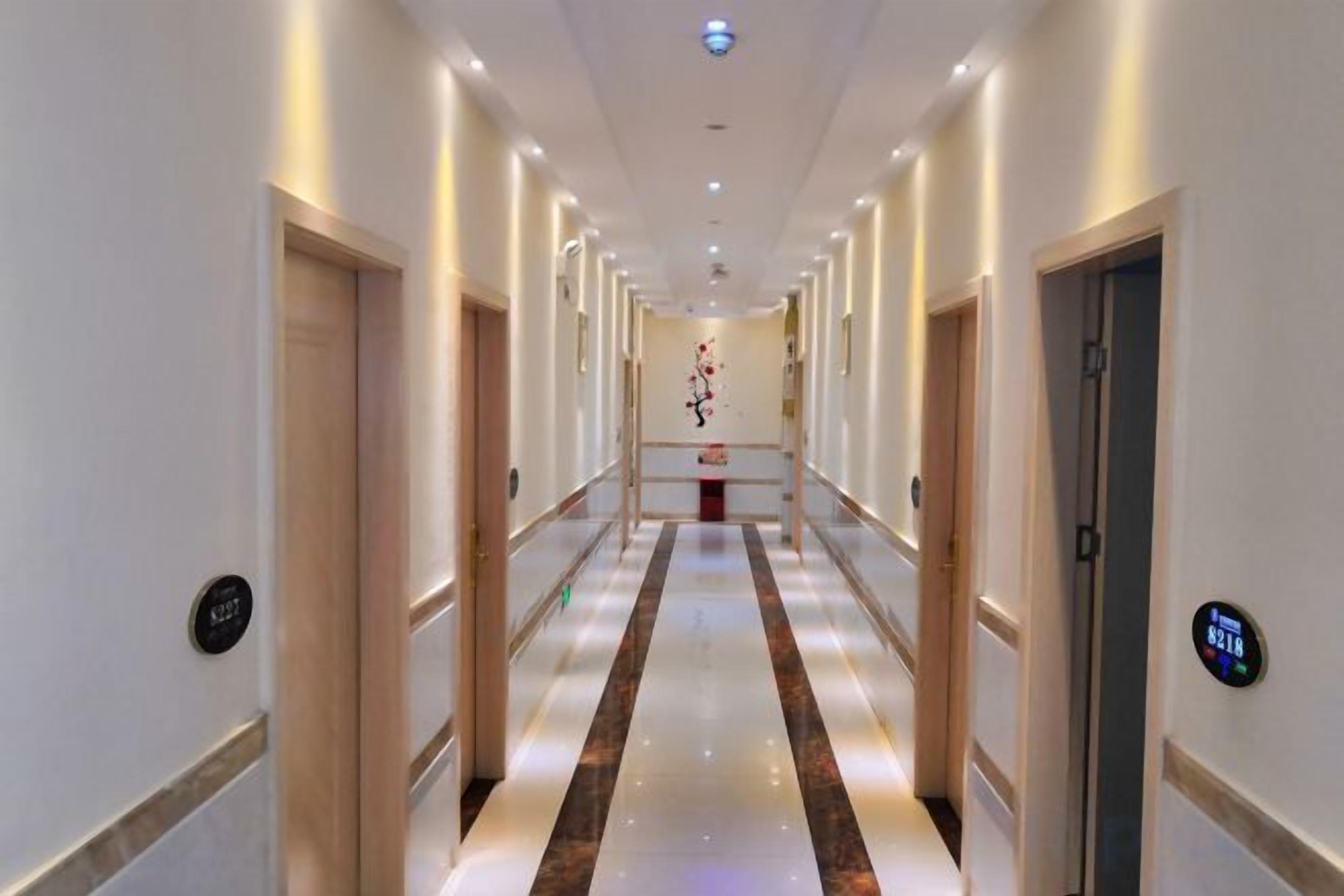 Passadís d'hotel amb portes a banda i banda, un camí central i un sostre amb il·luminació empotrada.