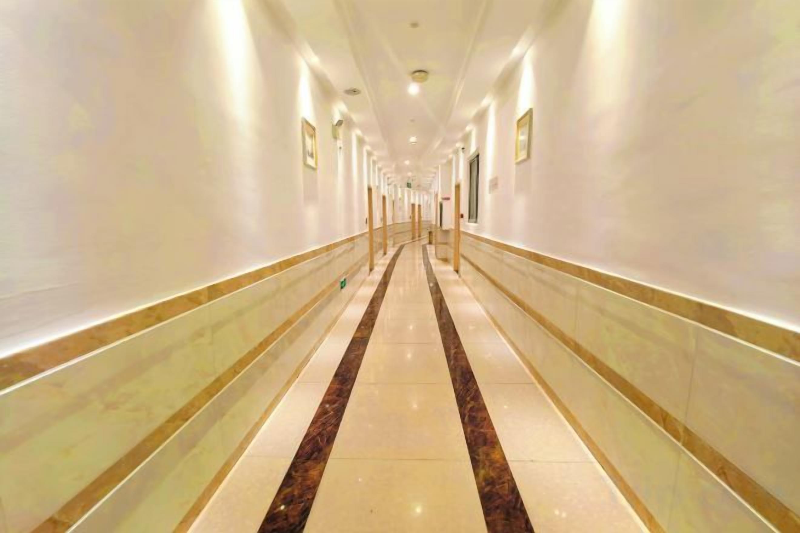 A long, well-lit corridor with a marble floor and walls, leading to a door at the end.