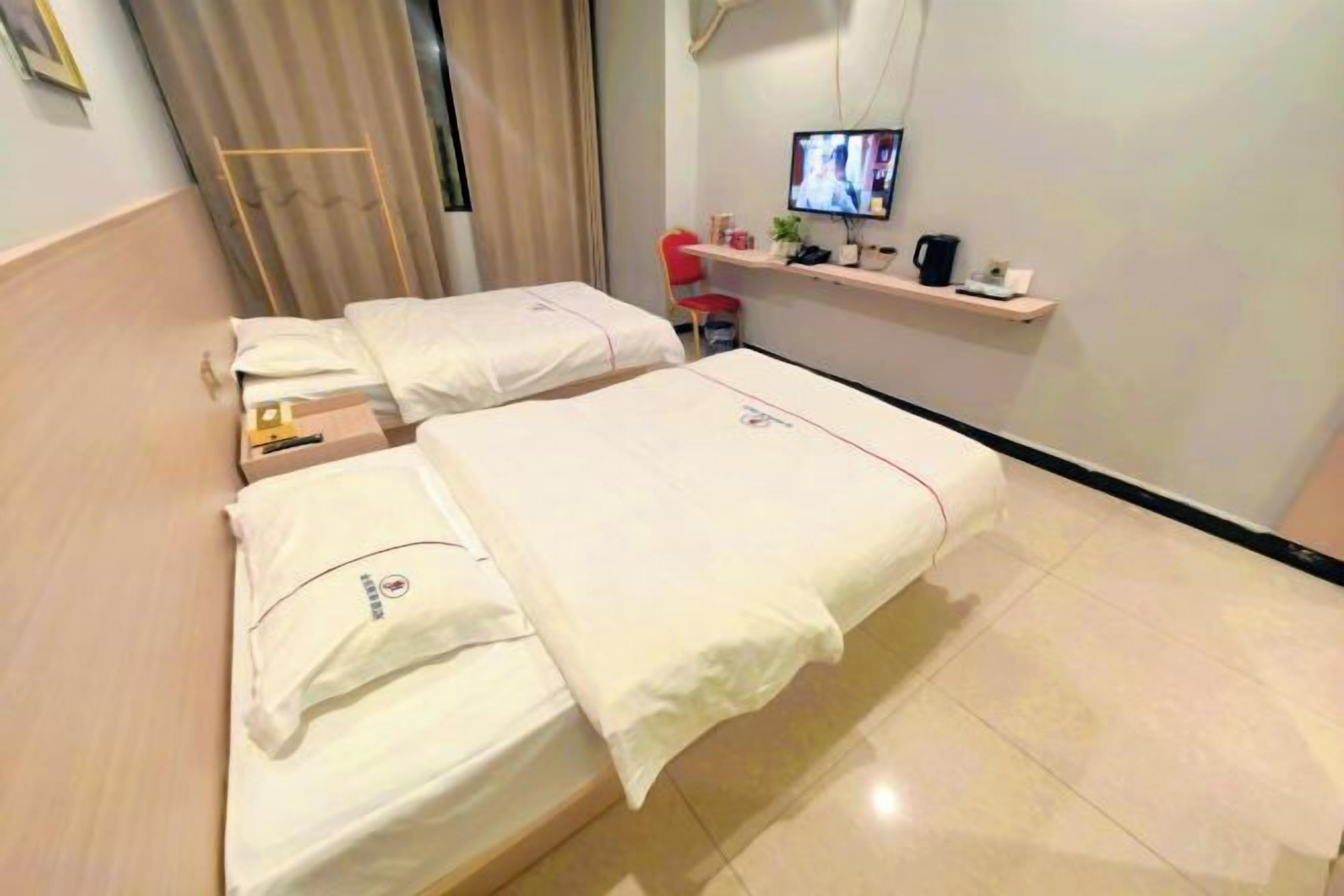 Ein Hotelzimmer mit zwei Betten, einem Fernseher auf einem Regal und einem kleinen Schreibtisch mit Stuhl.