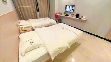 Ein Hotelzimmer mit zwei Betten, einem Fernseher auf einem Regal und einem kleinen Schreibtisch mit Stuhl.