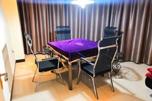 Un coin repas avec une table recouverte d’une nappe violette, quatre chaises et un rideau en arrière-plan.