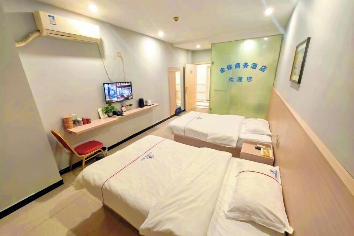 Une chambre d’hôtel avec deux lits, une télévision, une étagère avec des articles de toilette et une porte avec une pancarte verte.