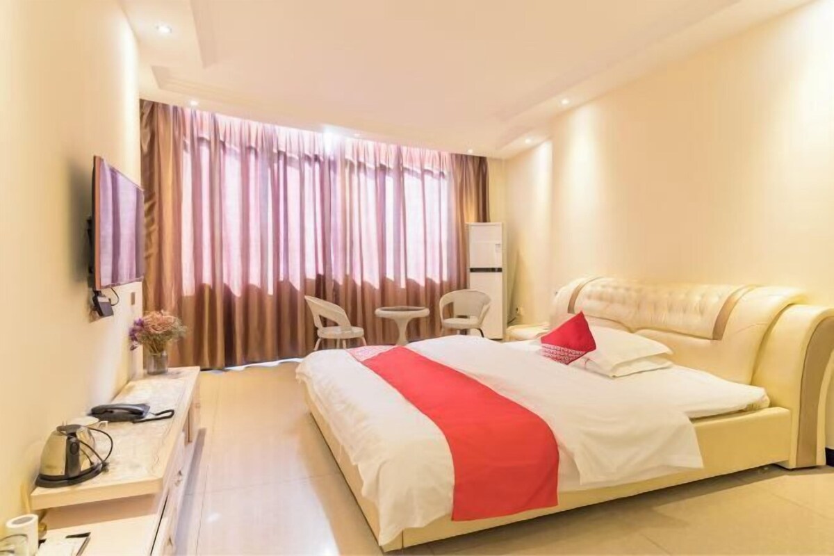 Une chambre d’hôtel avec un lit, un bureau avec un téléphone, une chaise, une petite table et un téléviseur fixé au mur.