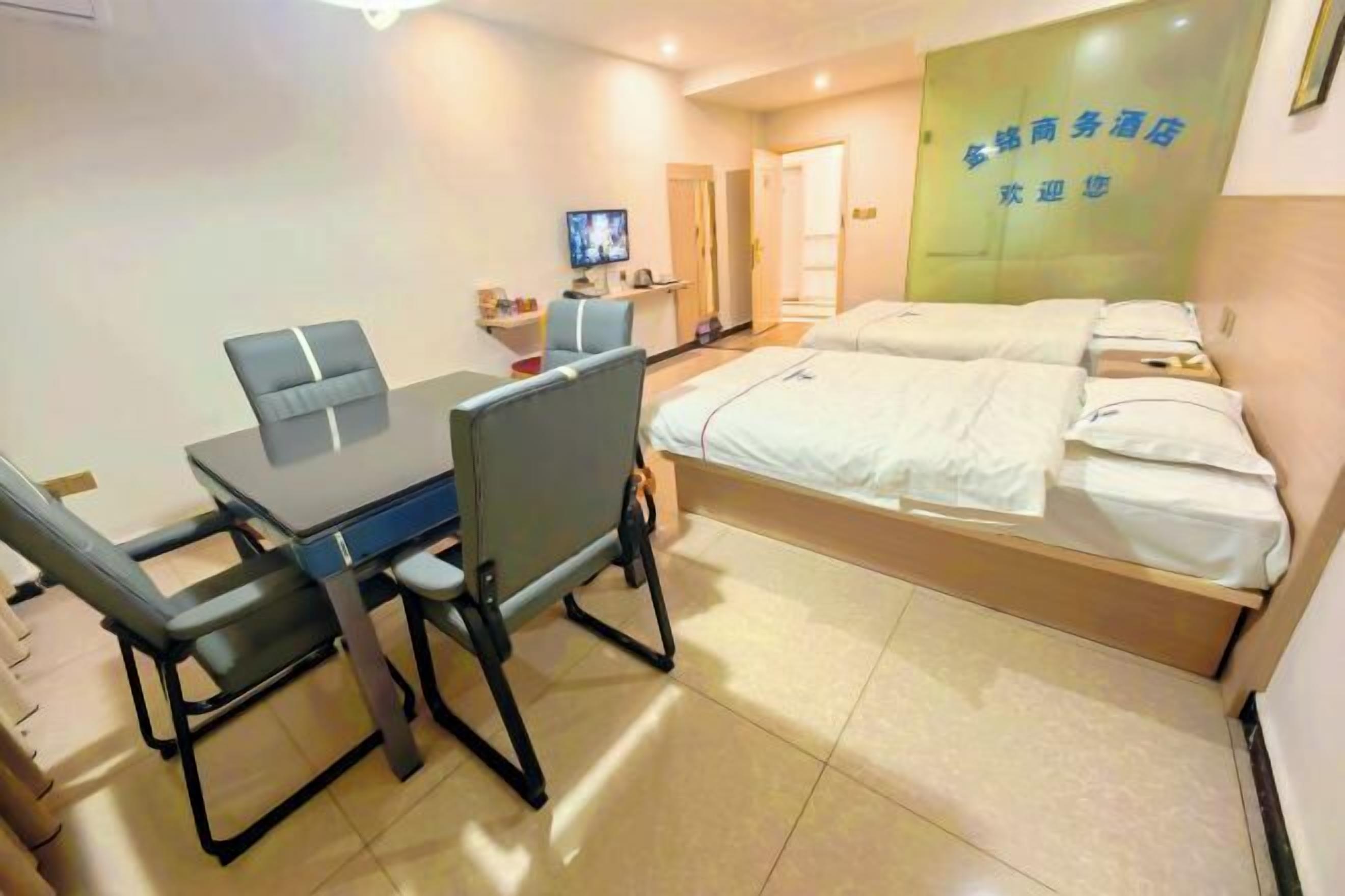 A hotel room with a bed, a desk, and a chair. There is a television on the desk and a door in the background.