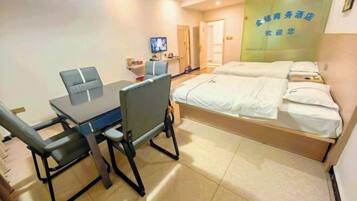 A hotel room with a bed, a desk, and a chair. There is a television on the desk and a door in the background.
