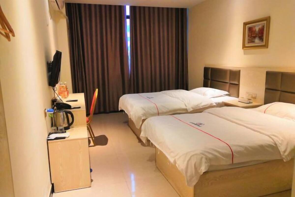 Hotellihuone, jossa on kaksi sänkyä, työpöytä, jossa on vedenkeitin, tuoli ja seinälle asennettu televisio.
