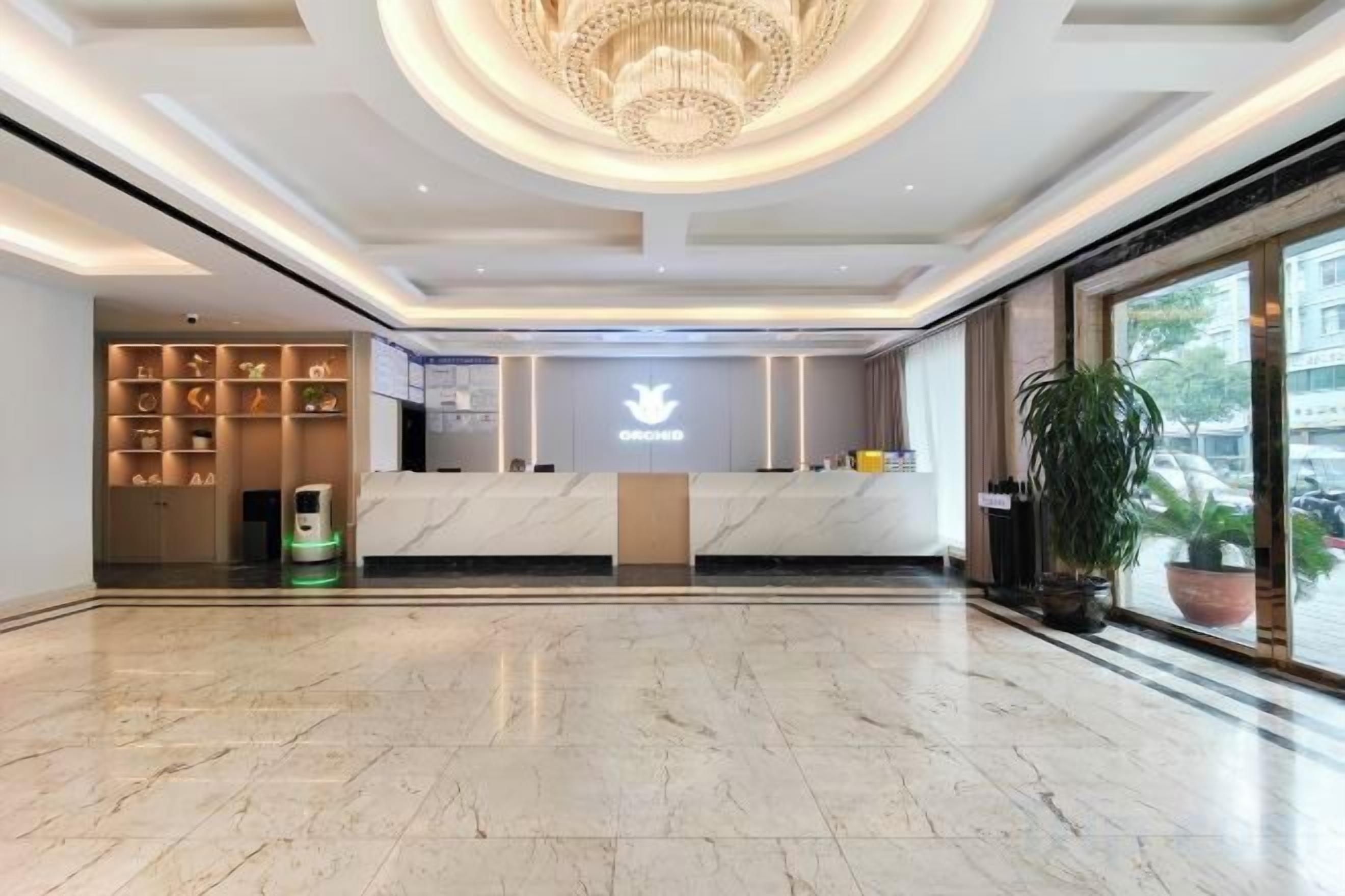 A hotel reception area with a marble floor, a chandelier, and a reception desk with a logo.