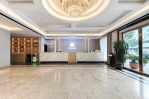 A hotel reception area with a marble floor, a chandelier, and a reception desk with a logo. - Fu Xuan Hotel (Xiushan County)